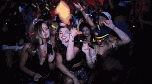 a group of women are dancing at a party in a dark room with their hands in the air .