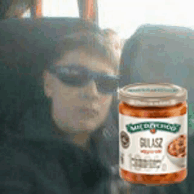 a man wearing sunglasses is sitting in a car next to a jar of salsa .