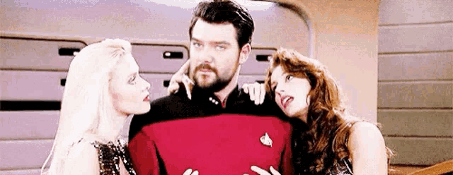 a man with a beard is surrounded by two women on a space ship .