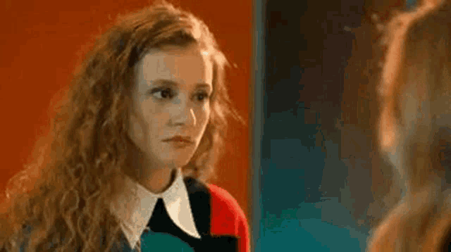 a young woman with curly hair is looking at another woman in a mirror .