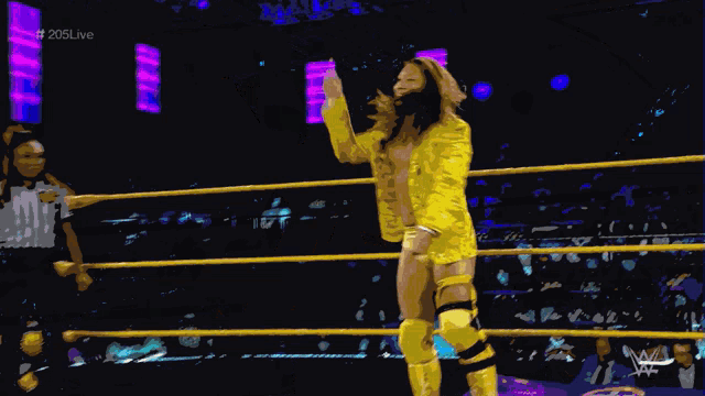a woman in a yellow suit is standing in a wrestling ring with the hashtag # 205live