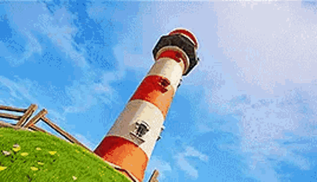 a red and white lighthouse is on top of a grassy hill .