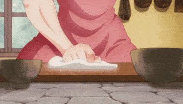 a woman in a pink apron is kneading something on a wooden table
