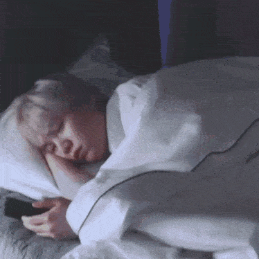 a person is sleeping in a bed and looking at a cell phone