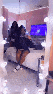 a woman is sitting on a bed in front of a mirror taking a picture of herself .
