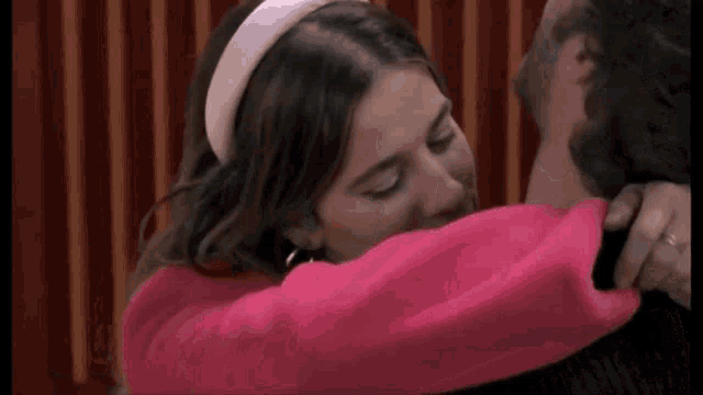 a man and a woman are hugging each other . the woman is wearing a pink sweater and a white headband .