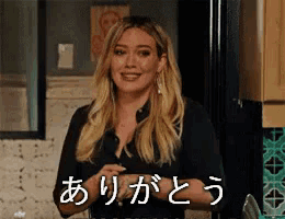 a woman in a black shirt is smiling in a kitchen with chinese writing on the wall .