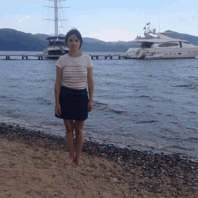 a woman stands on a beach in front of a large boat