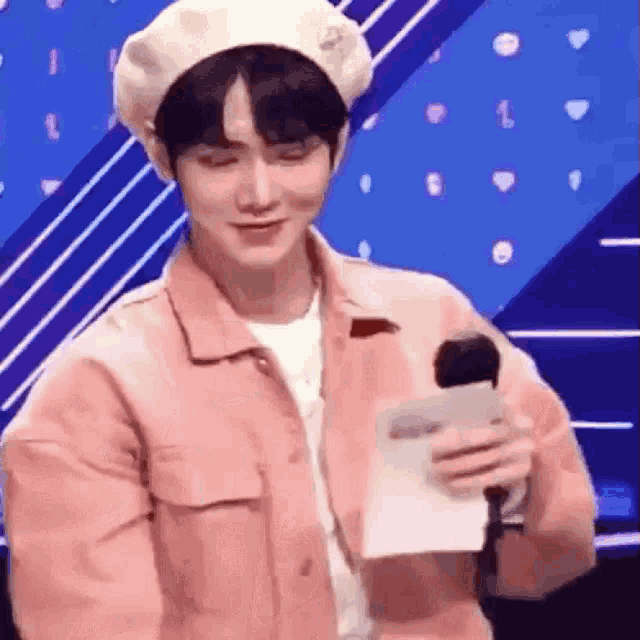 a man wearing a pink jacket and a white hat is holding a microphone .