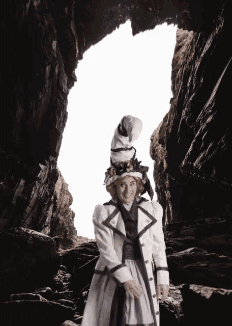 a woman in a white coat and purple striped skirt is standing in a cave