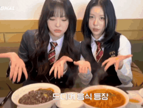 two girls in school uniforms are sitting at a table with bowls of food and korean writing on the table