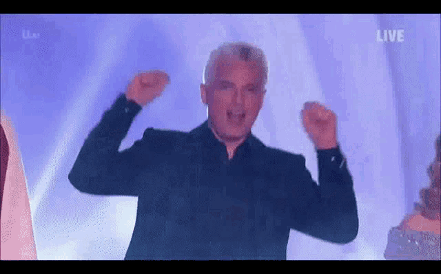 a man in a black suit is standing on a stage with his arms in the air .