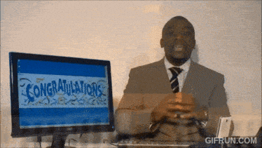 a man in a suit and tie stands in front of a computer screen that says " congratulations "