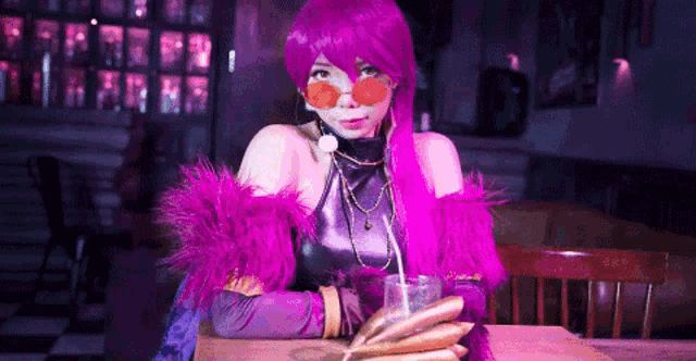a woman in a purple wig is sitting at a table drinking from a glass .