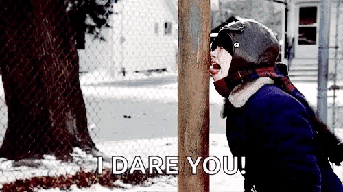 a girl in a helmet is standing in the snow next to a tree and talking to someone .