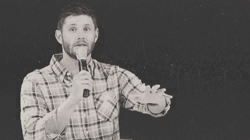 a man in a plaid shirt is holding a microphone and giving a speech .