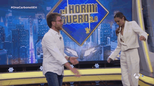 a man and woman are dancing in front of a sign that says hormi guero 3.0