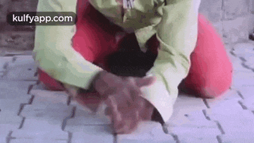 a person is kneeling down on a brick floor with their hands folded .