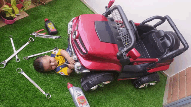 a little boy laying on the grass next to a toy car with castrol oil