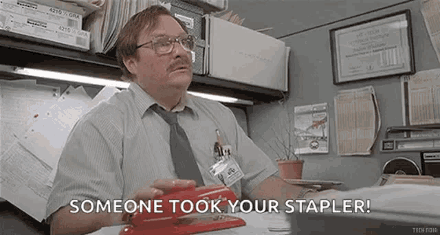 a man is sitting at a desk with a stapler in his hand .