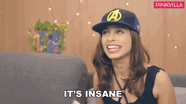 a woman wearing an avengers hat is sitting on a couch and says it 's insane
