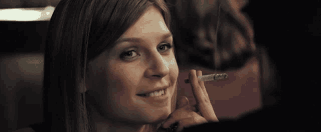 a woman is smoking a cigarette and smiling for the camera