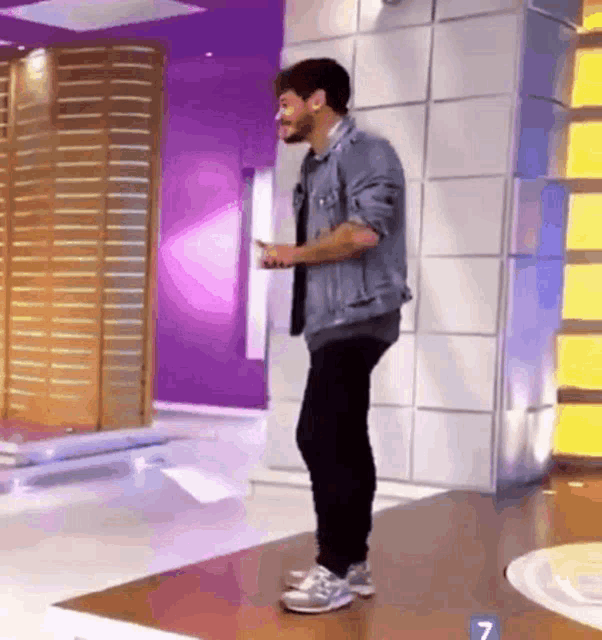 a man in a denim jacket is standing in front of a purple wall with the number 7 in the corner