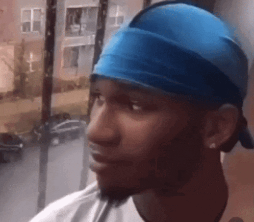 a man wearing a blue headband and a white shirt is looking out a window .