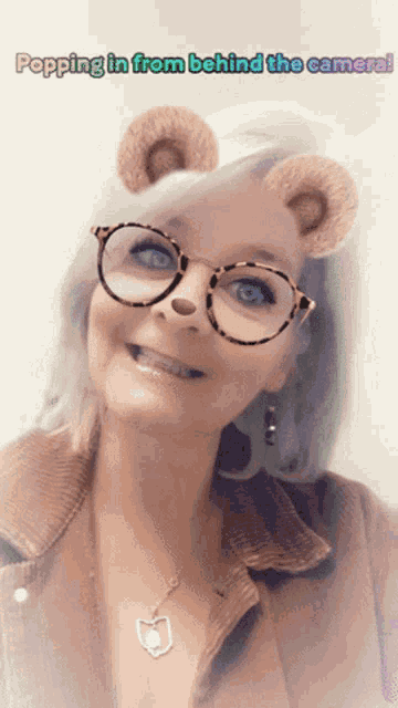 a woman wearing glasses and a necklace with the words popping in from behind the camera