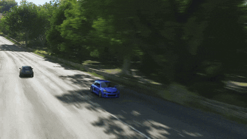 two blue cars are driving down a road with trees on the side