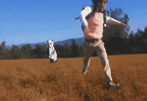 a man and a panda bear are running through a grassy field
