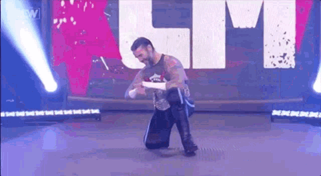 a wrestler is kneeling down on a stage in front of a sign that says lm .
