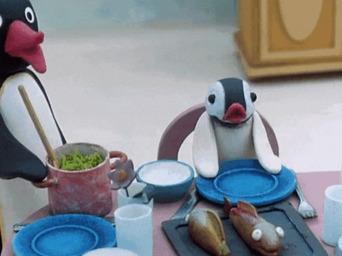 two stuffed penguins are sitting at a table with plates and a pot of food .