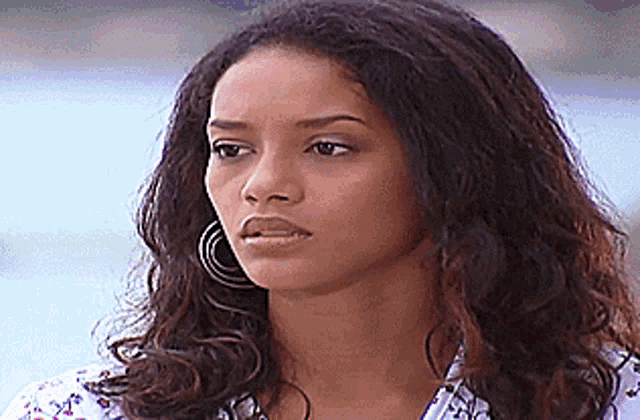 a woman with curly hair is wearing hoop earrings and a white shirt