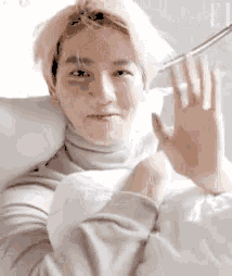 a young man with blonde hair is laying in a bed with his hand up .