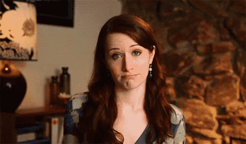 a woman with long red hair is making a funny face in front of a stone wall .