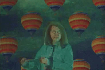 a woman in a green jacket stands in front of a pattern of hot air balloons