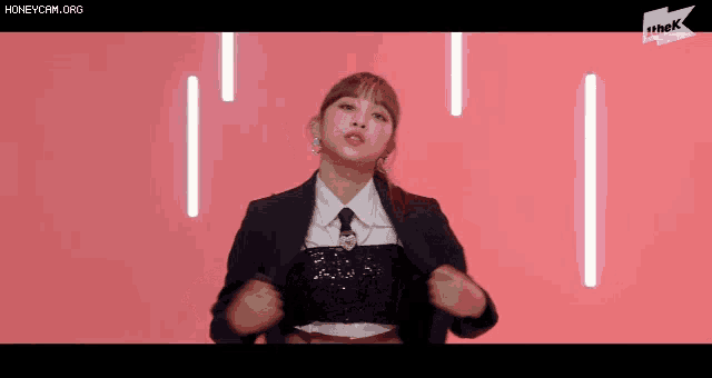 a woman in a suit and tie is standing with her hands on her hips in front of a pink background