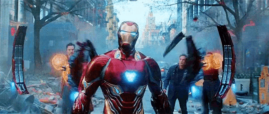 iron man is standing in the middle of a destroyed city with a group of people .