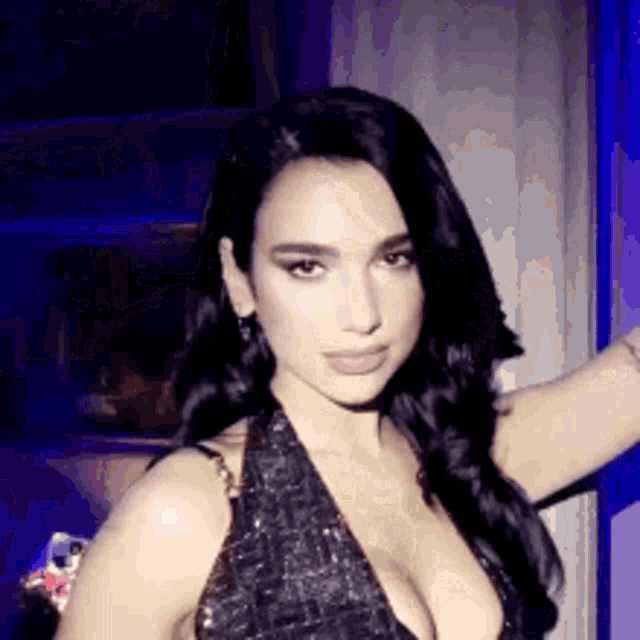 a woman in a black dress with a plunging neckline is standing in a dark room .
