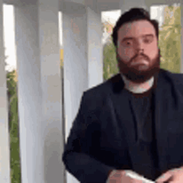 a man with a beard wearing a suit and tie is standing in a room .