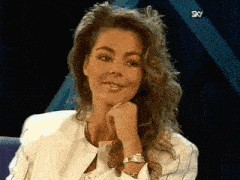 a woman with long curly hair is wearing a watch and a white jacket and smiling .