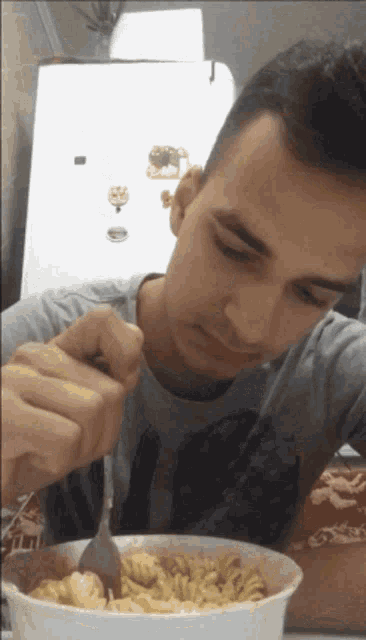 a man is eating a bowl of macaroni and cheese with a spoon
