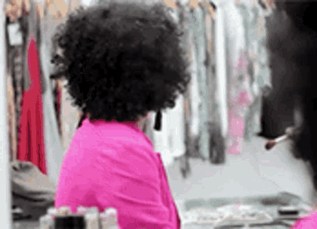 a woman in a pink shirt is sitting in front of a mirror .