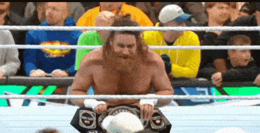 a man with a beard is sitting in a wrestling ring with a crowd watching .