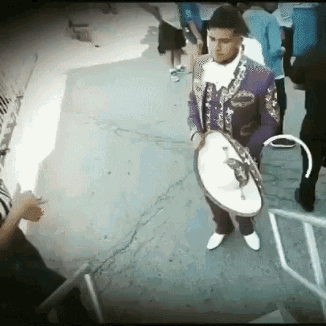 a man in a purple suit is holding a sombrero while standing on a sidewalk .