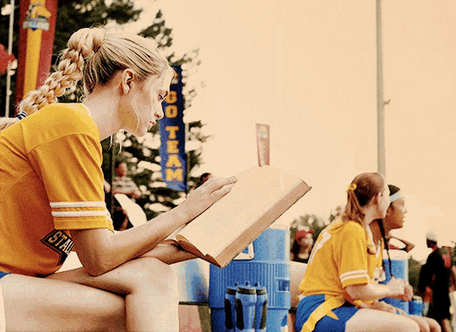 a woman wearing a yellow shirt with the word state on the sleeve reads a book