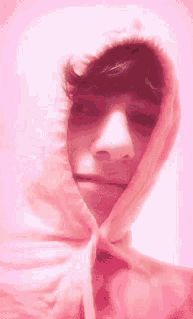 a young man is wearing a pink hoodie and making a funny face .
