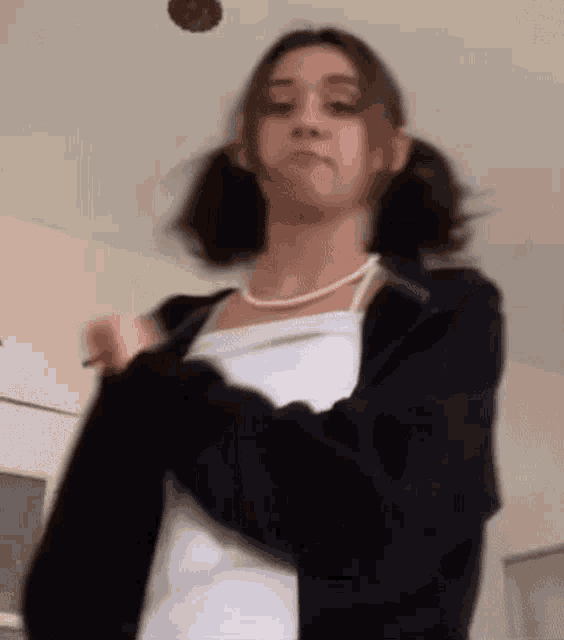a young woman wearing a white tank top and a black jacket is standing in a room .