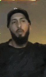 a man with a beard wearing a la hat waves his hand